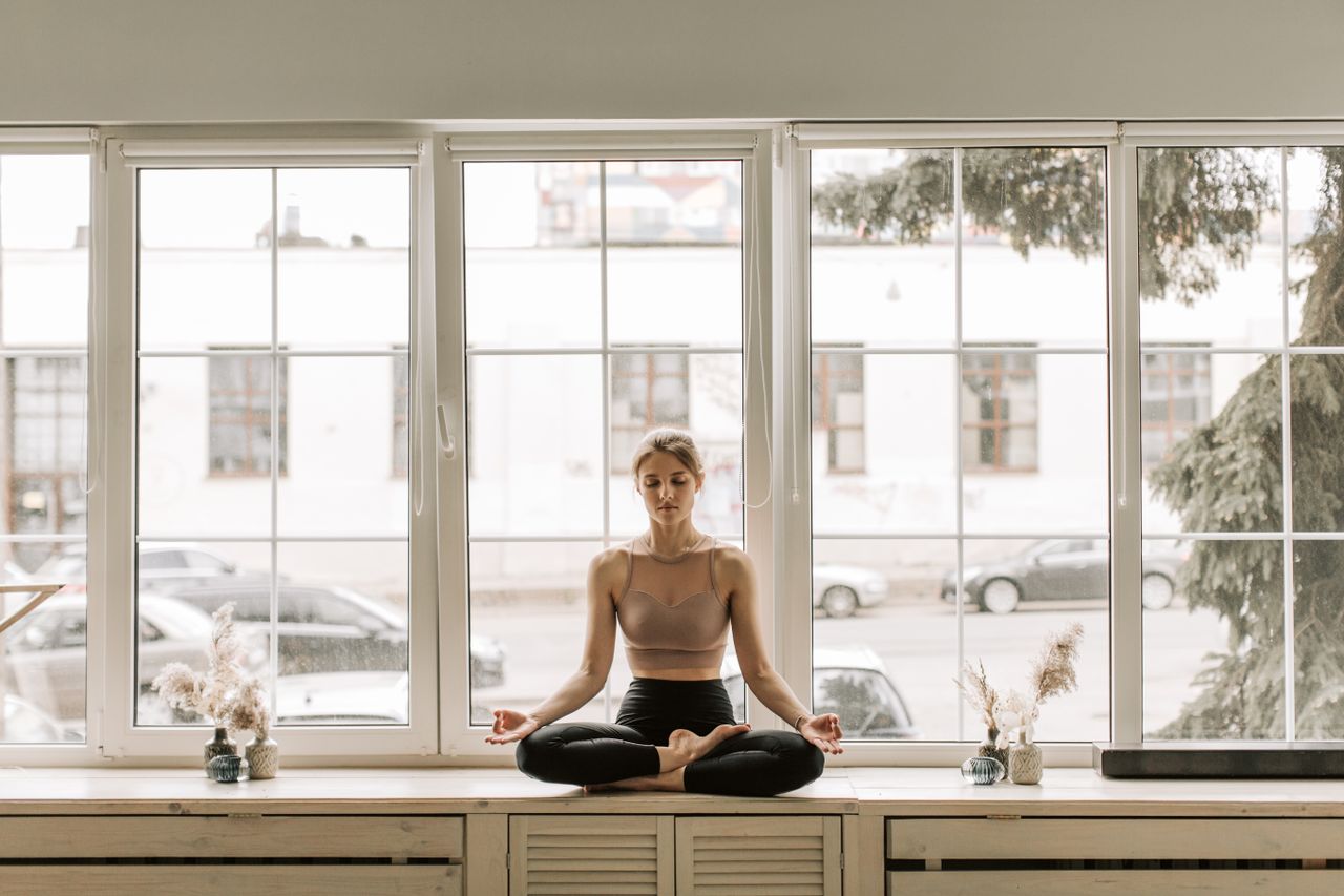 Calm woman practicing meditation on a windowsill indoors, embracing mindfulness and relaxation.