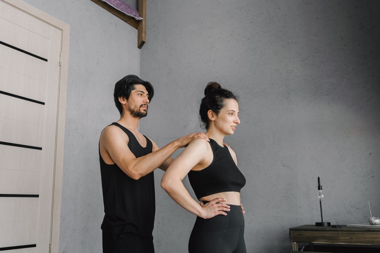 Fitness coach assisting woman with stretching exercises indoors.